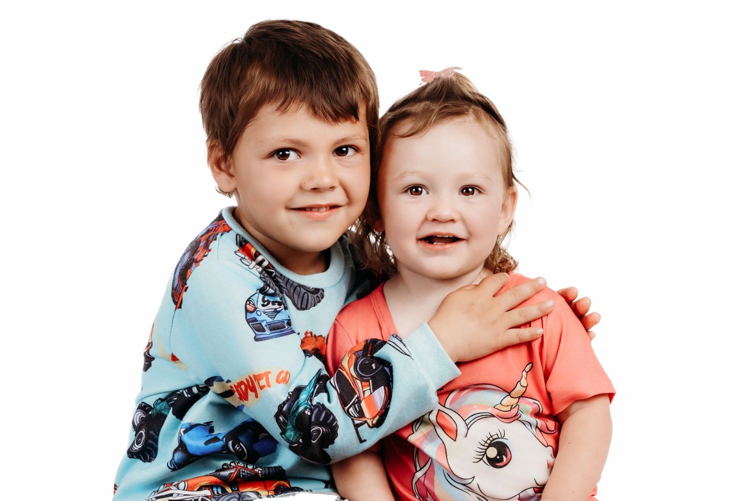 Two young children wearing festive holiday outfits pose together against a colorful painted background.