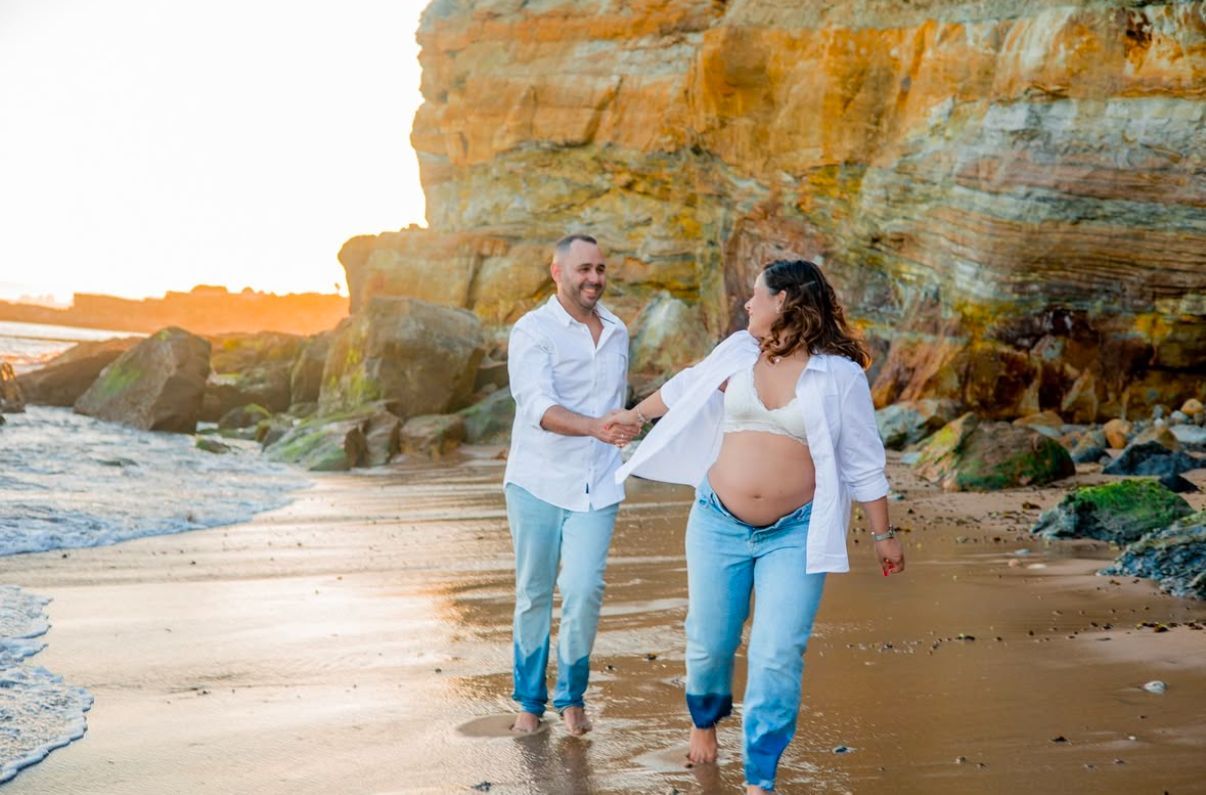 Couple walking along scenic beach with dramatic cliffs during golden hour.