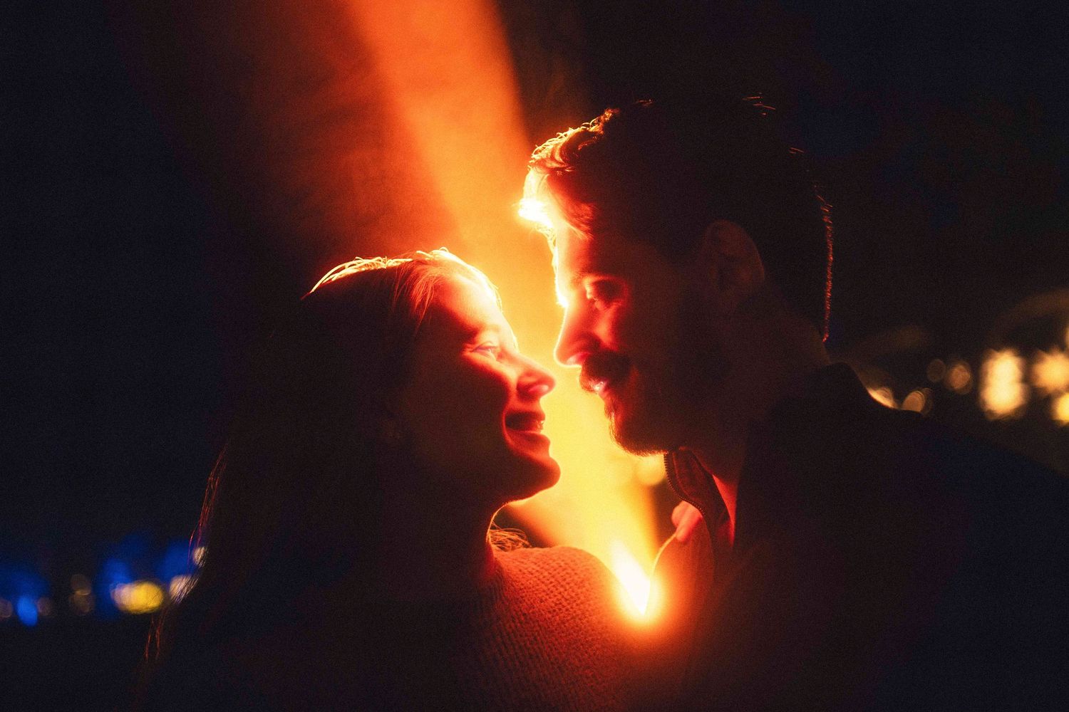 A silhouetted couple in profile faces each other with a glowing orange light between them at night at descanso gardens pasadena.