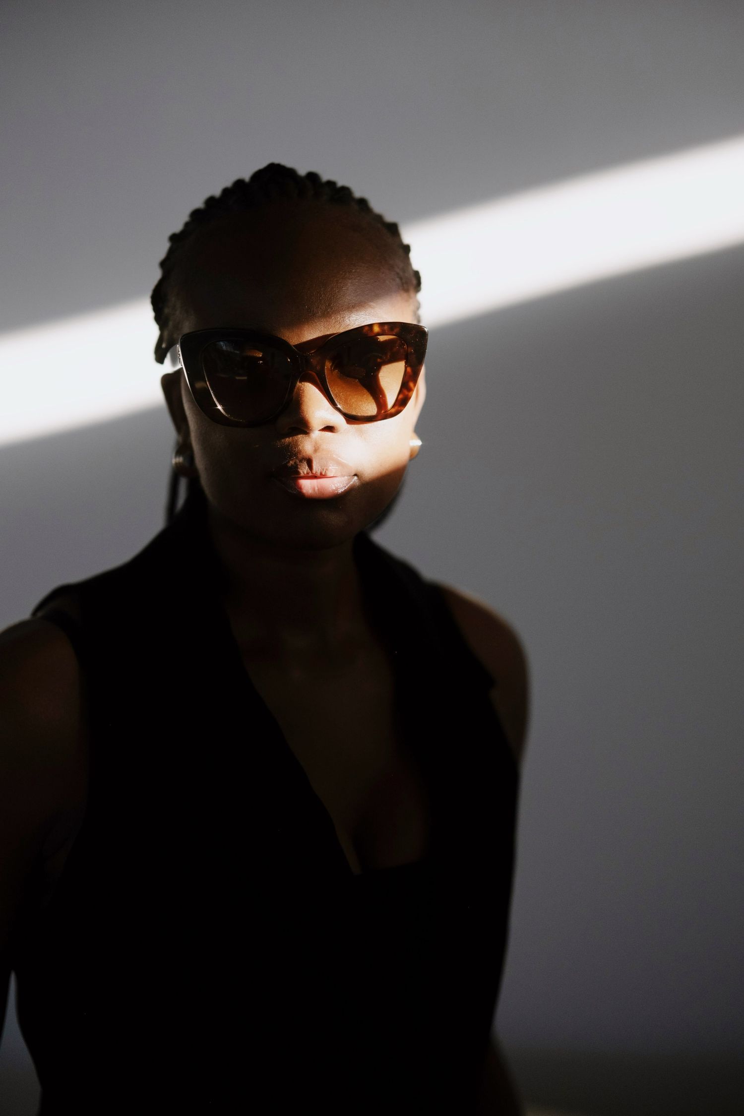 Black woman in oversized brown sunglasses poses dramatically in studio lighting.
