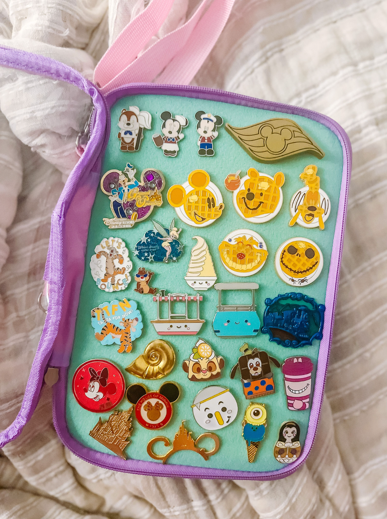 Purple and pink Disney pin collecting case filled with character and attraction themed pins.