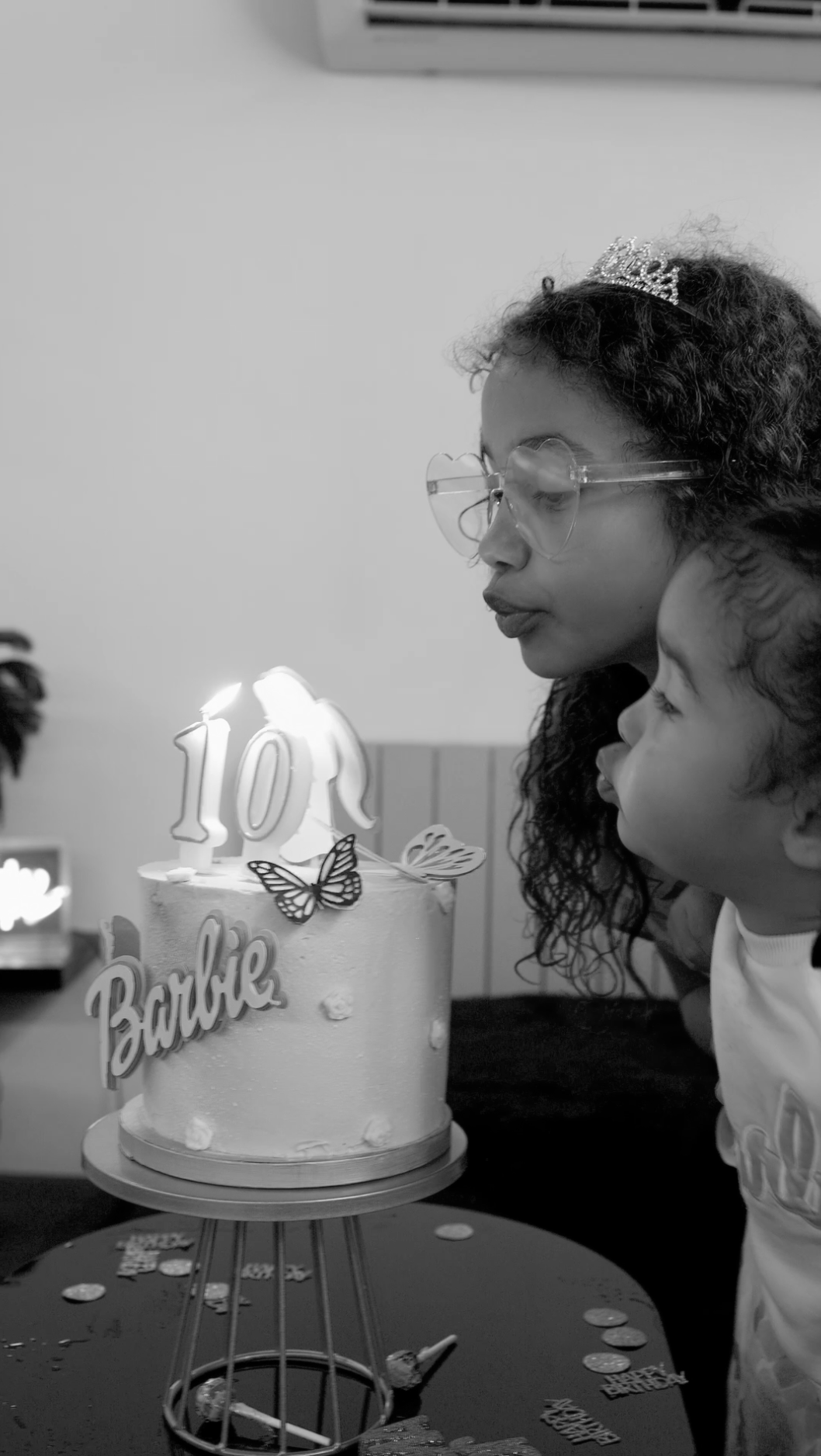 A pink birthday cake with lit number 10 candle and butterfly decorations sits on a table at a celebration.