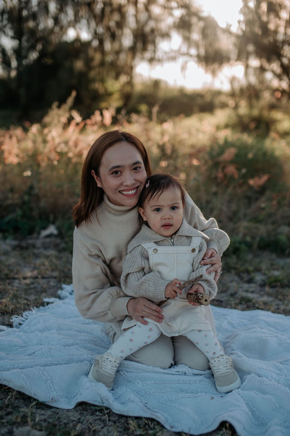 A heartwarming outdoor photoshoot of a parent and child sitting together on a light blue blanket in autumn afternoon light.