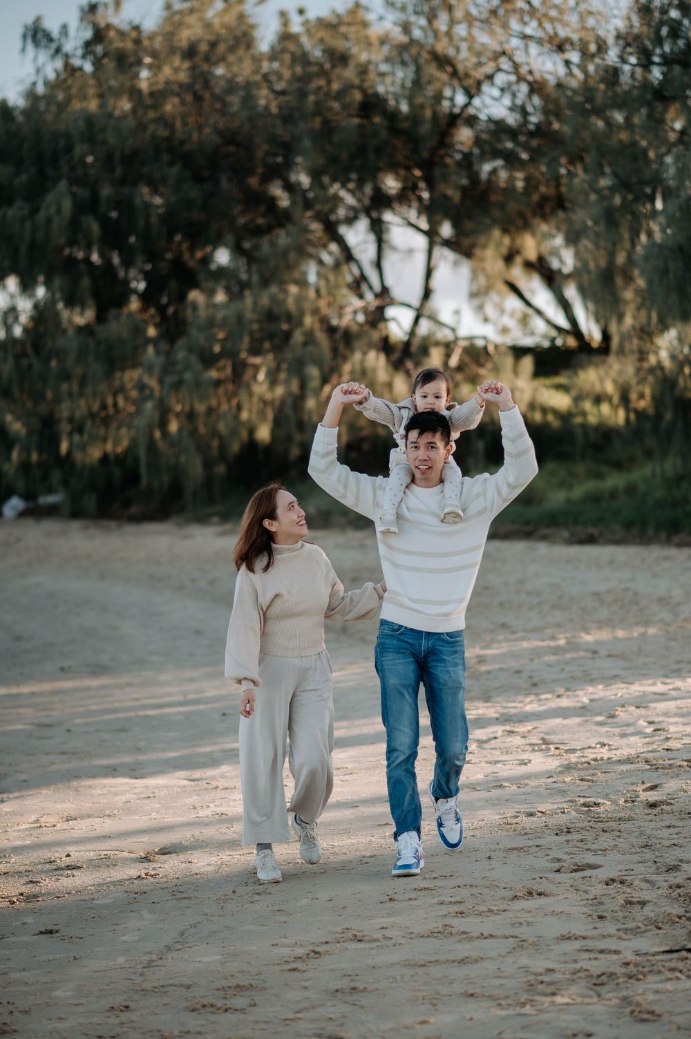 A couple walks together on a sandy beach path under trees during golden hour.