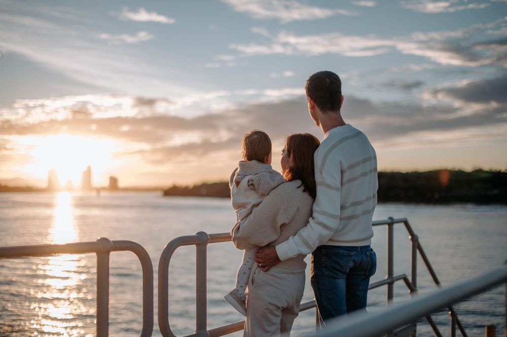 Family in matching light-colored outfits watching sunset together on pier by waterfront.