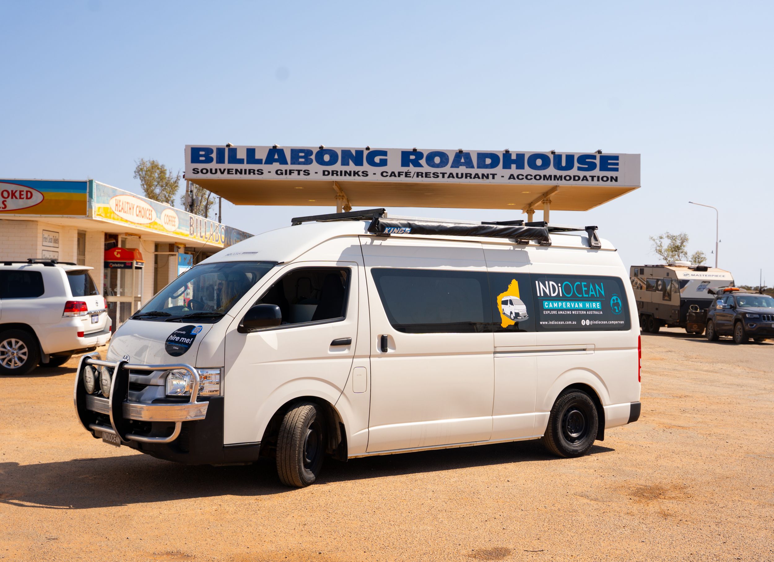 White van parked outside the Billabong Roadhouse in a dusty outback location.