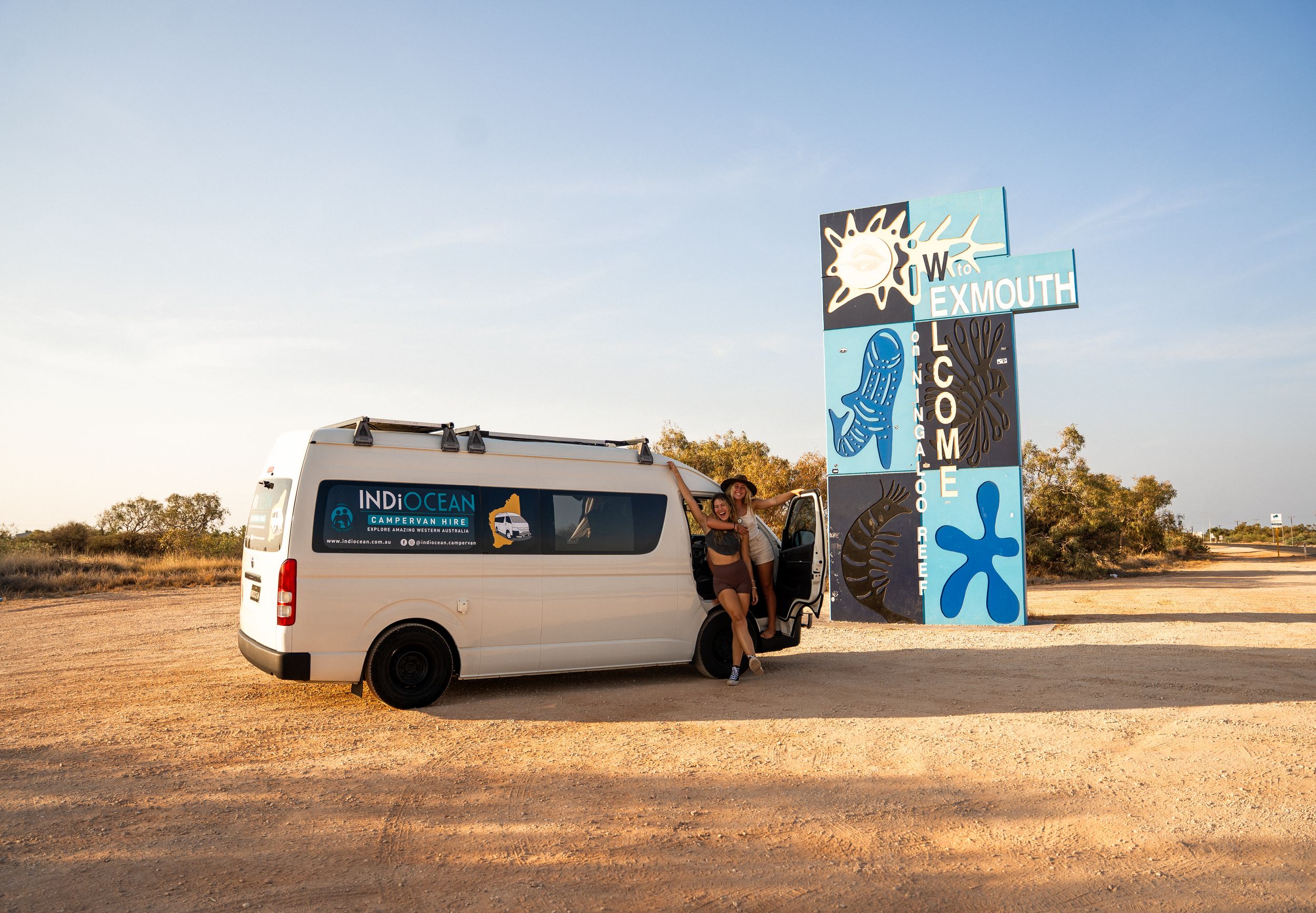 White camper van parked next to a large outdoor mural in a desert setting.