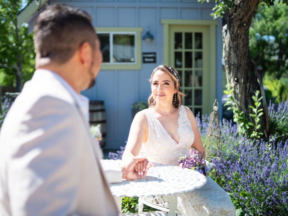 Wedding couple sits at an outdoor table surrounded by blooming purple lavender on a sunny summer day.