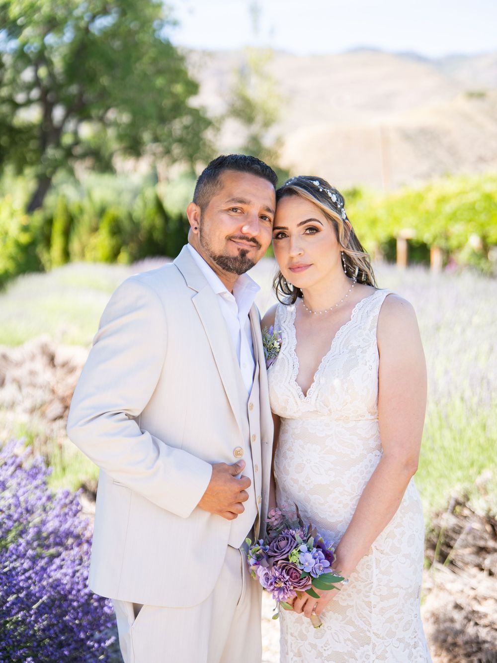 Romantic outdoor wedding portrait in cream and white attire with a lavender bouquet against a mountain landscape.