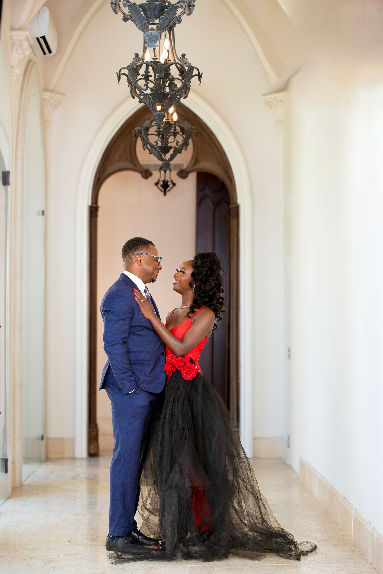 Romantic couple embracing under ornate chandelier in elegant hallway.