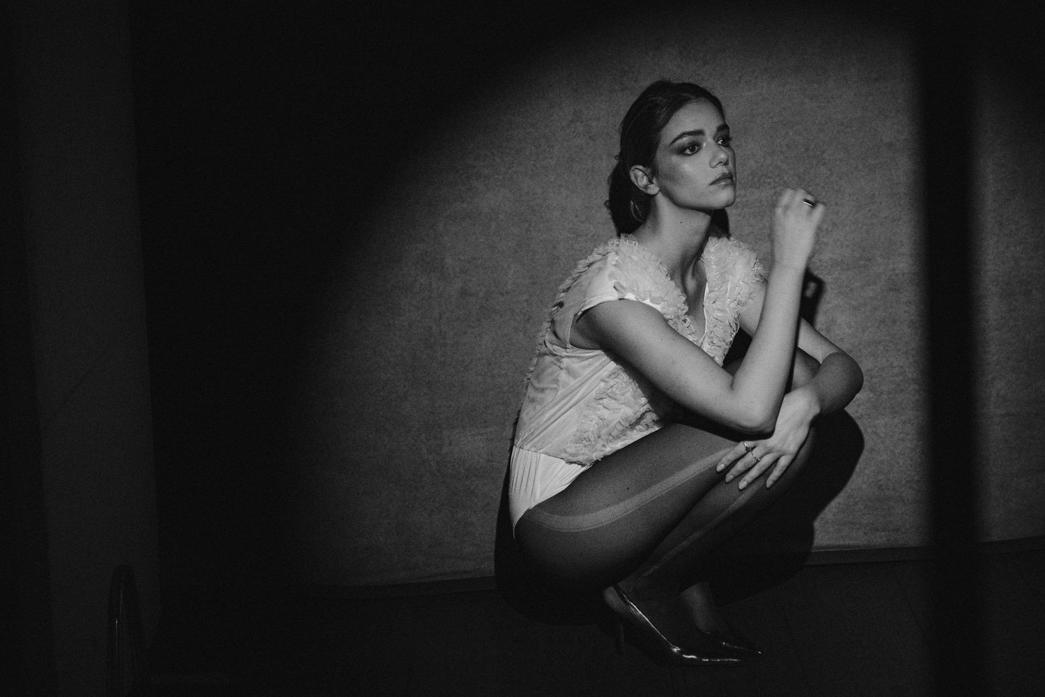 Moody black and white portrait showing figure in lace dress in contemplative crouch position.