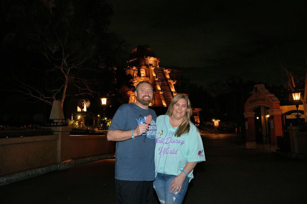 Couple smiling at night outside the Haunted Mansion attraction at a Disney theme park.