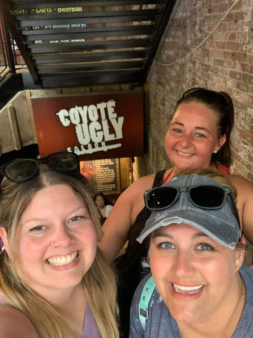 Three women smiling for a selfie outside Coyote Ugly Saloon bar entrance.