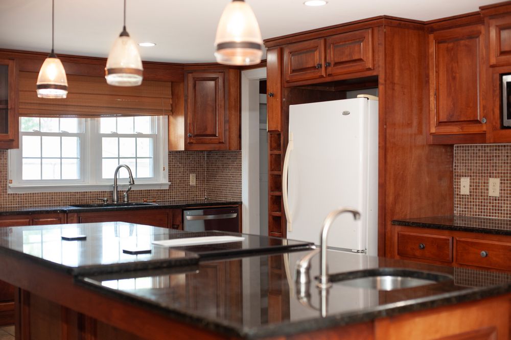 Modern kitchen with cherry wood cabinets, black granite countertops, and pendant lighting over a large center island.