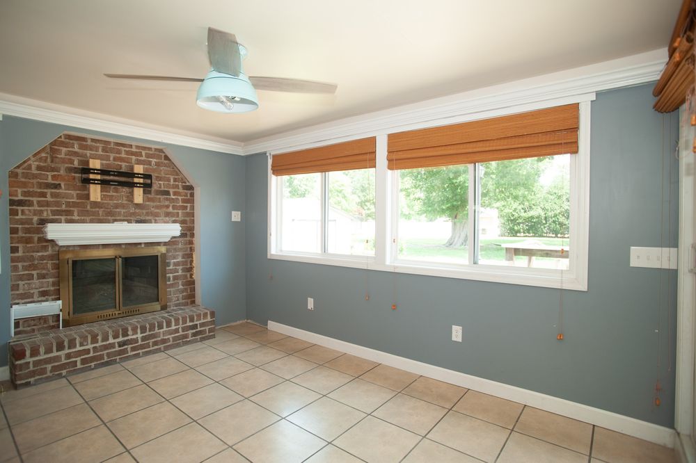 Living room with brick fireplace, blue-gray walls, tile flooring and large window with bamboo shades.