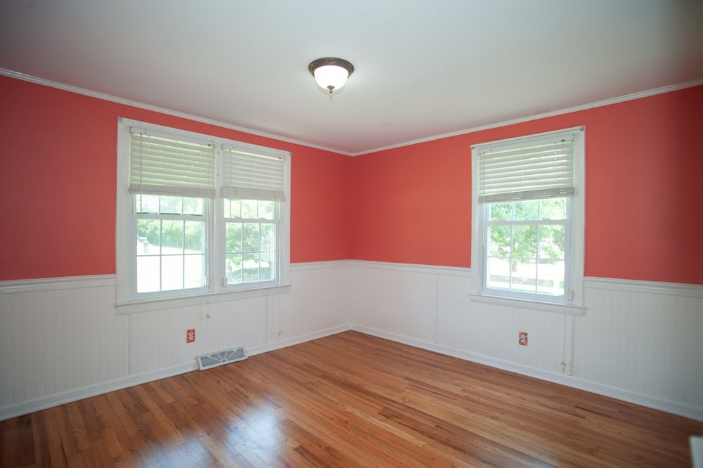 Empty bedroom with coral pink and white walls, hardwood floors, and two white-trimmed windows with blinds.