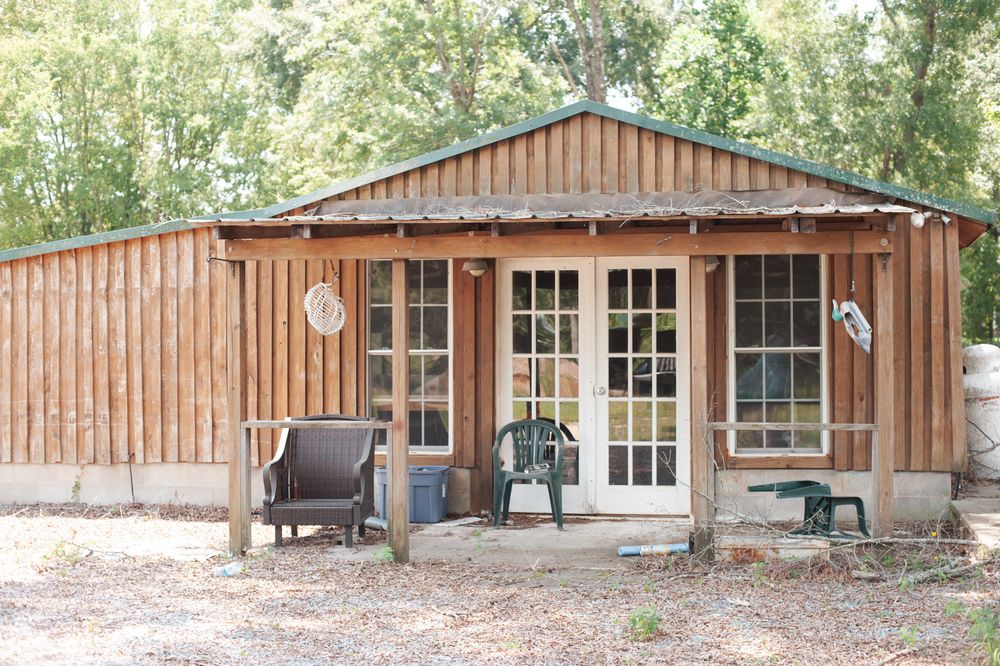 A rustic wooden cabin with French doors and outdoor seating sits in a wooded area.