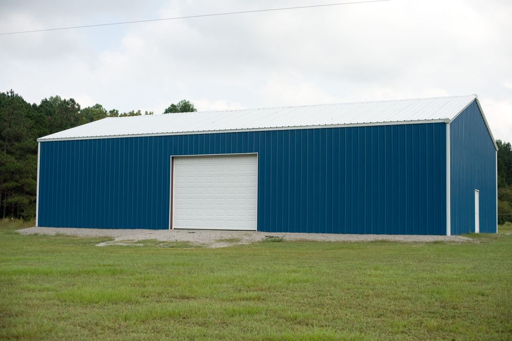 Large blue metal storage building with white trim and roll-up door situated on a grassy field.