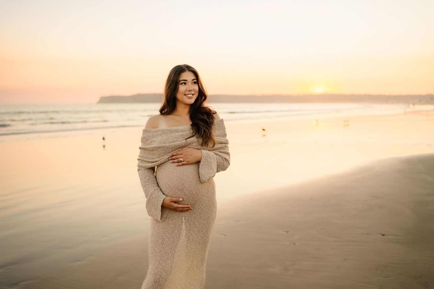 woman in sheer knit dress holds belly on Ventura beach during sunset maternity photoshoot by Thousand Oaks and Santa Barbara photographer