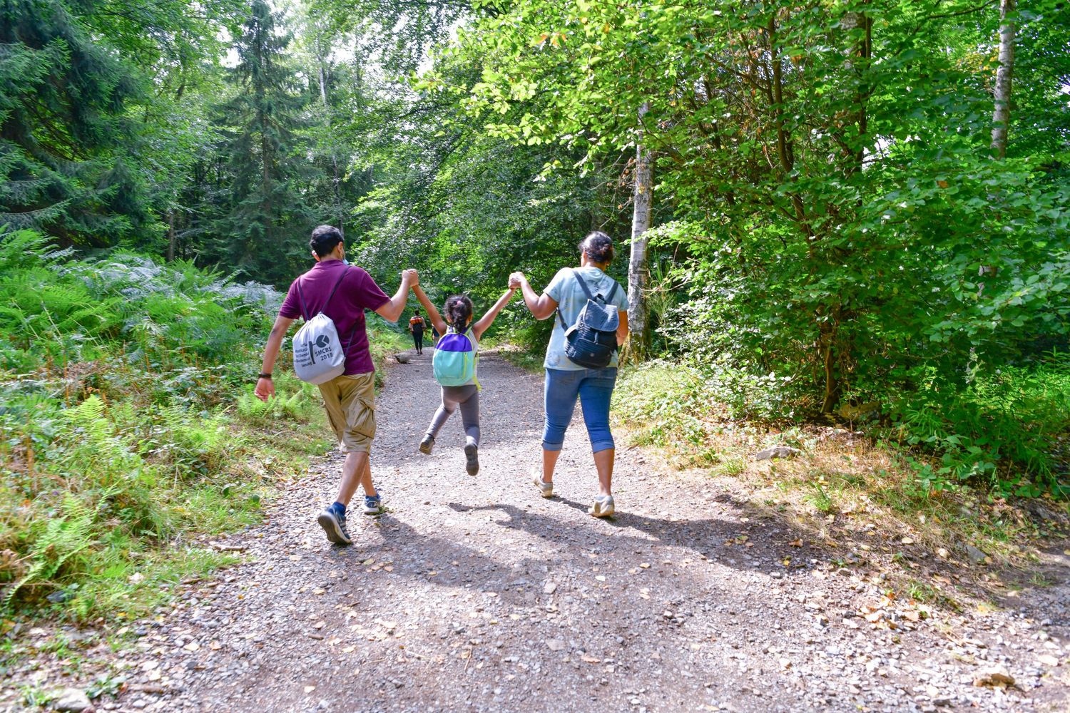 Three people enjoy a summer hike together on a forest trail surrounded by lush green trees.