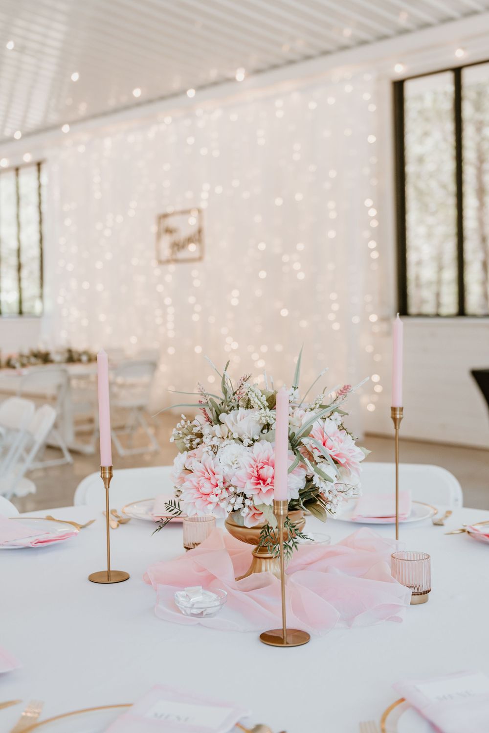 Romantic wedding table setting with pink florals, candles and twinkle lights in background.
