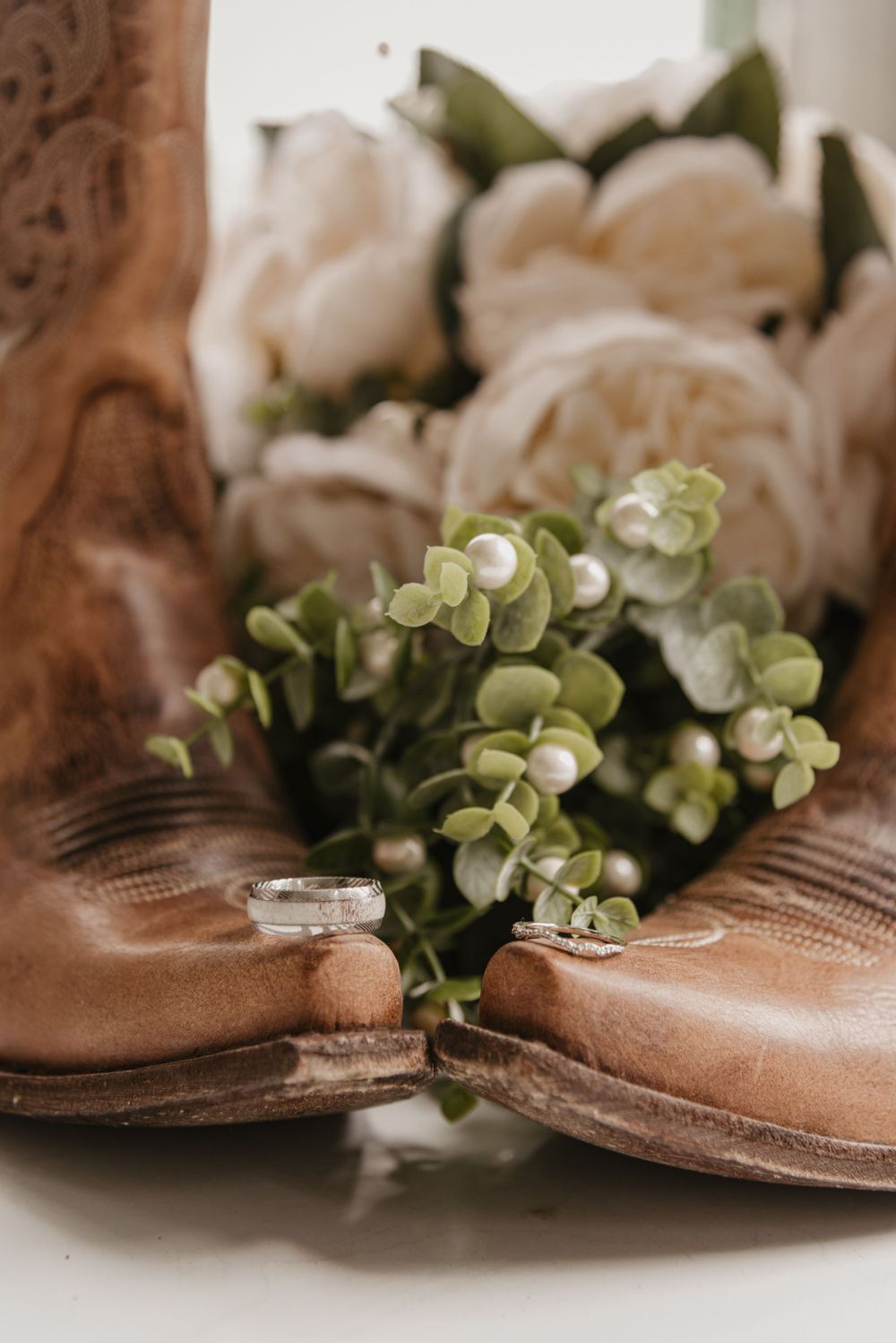 Brown leather boots with delicate greenery and white roses in soft natural light.