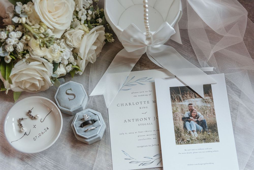 Wedding stationery and rings displayed with white roses and delicate veil details.