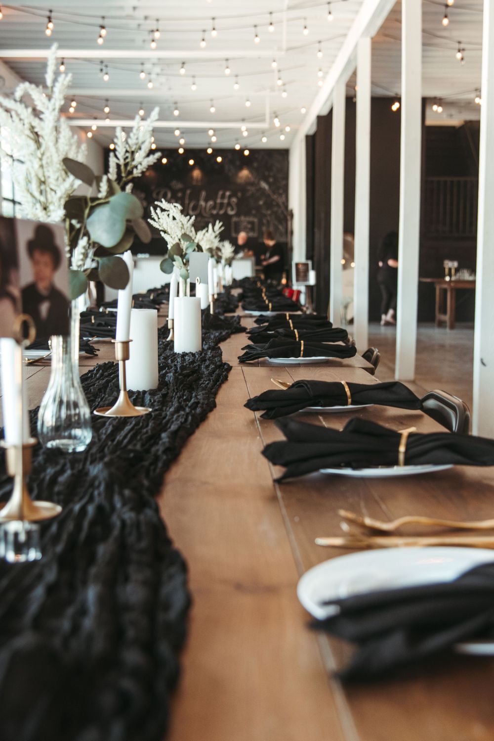 Elegant wedding reception table with black runners, candles and string lights overhead.