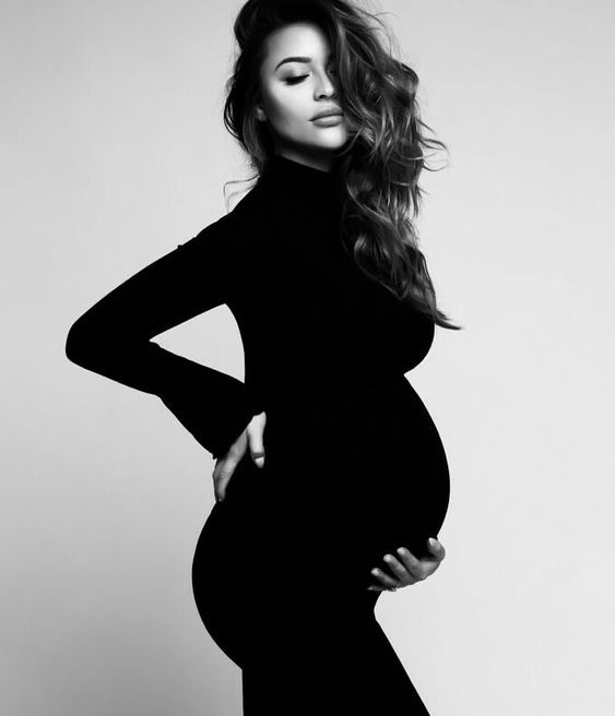 Black and white dramatic maternity portrait showing profile pose in fitted black dress.