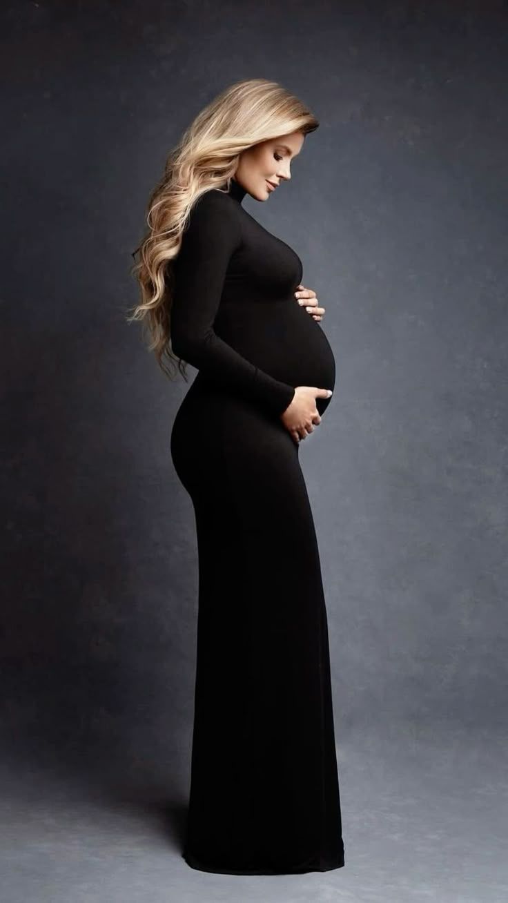 Elegant maternity portrait of woman in long black dress against dark background.