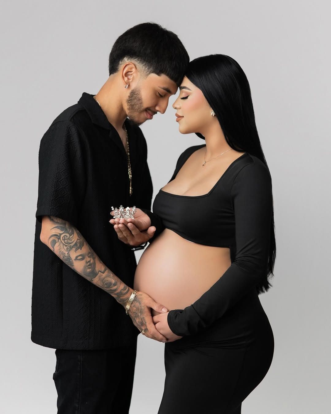 Intimate maternity photo of couple in black clothing against white background.