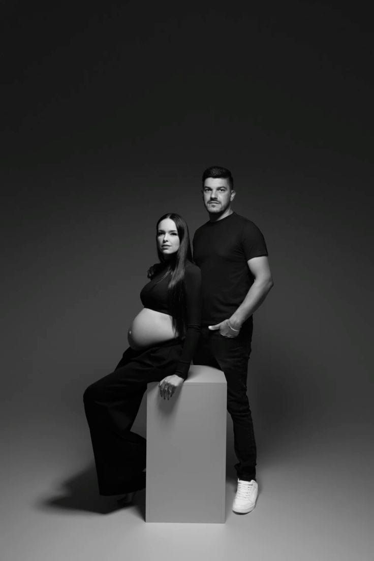 Studio maternity portrait with couple in black clothing posed with white geometric prop.
