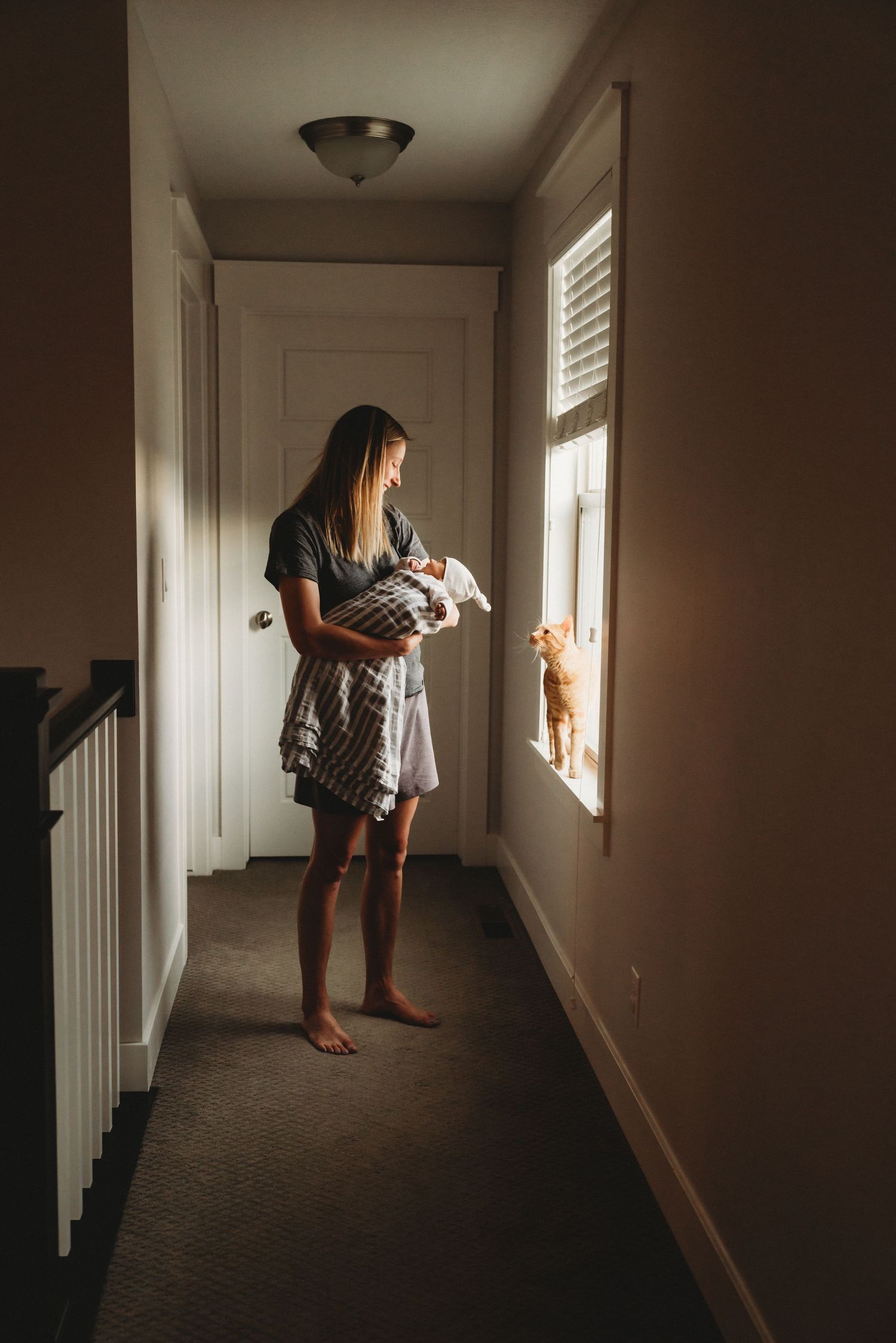 Silhouette of person holding baby while standing in hallway near window with natural light.