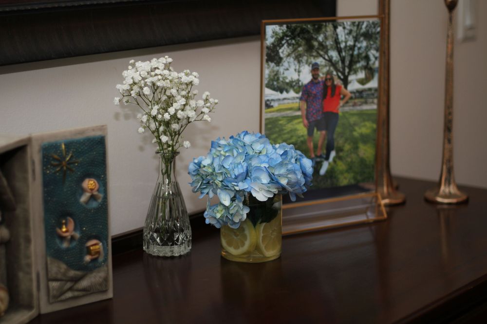 Table display with blue hydrangeas and white flowers in vases next to a framed photograph.