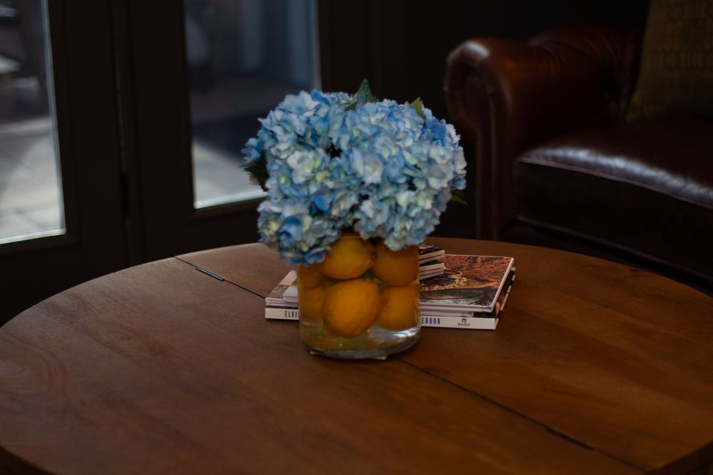 Wooden dining table decorated with blue hydrangeas and oranges in rustic farmhouse setting creates warm ambiance.
