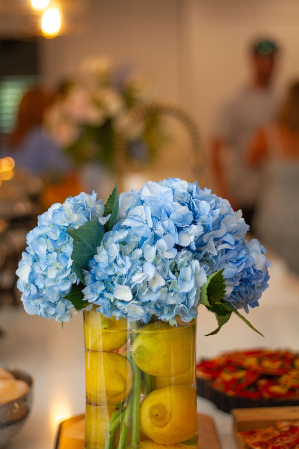 Blue hydrangea flowers arranged in a clear vase filled with fresh lemons.