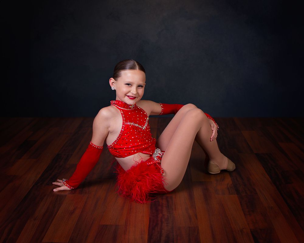 A collection showing dance poses performed on a dark hardwood floor in a flowing red costume and black shoes.
