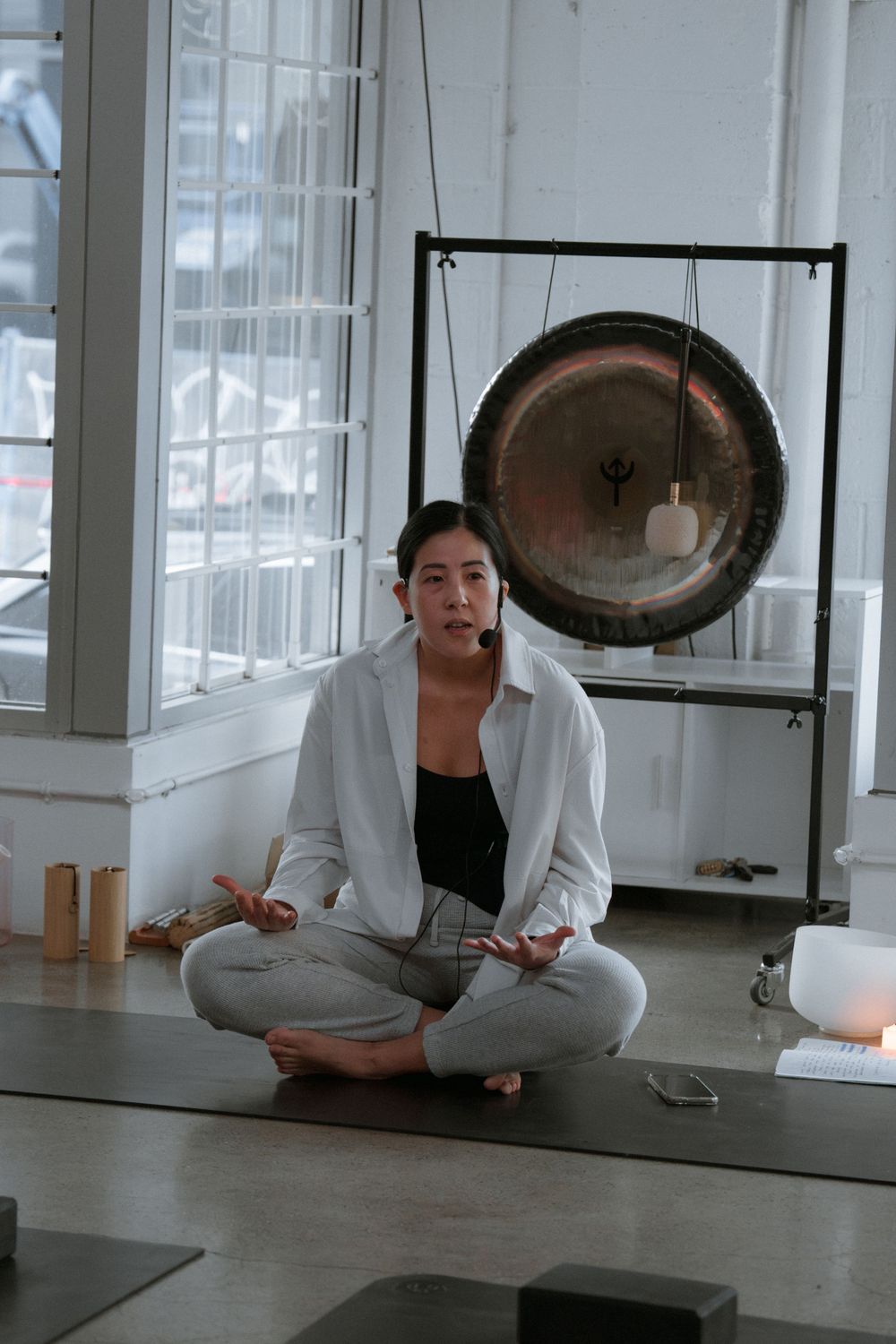 Person in white clothing stretches and performs yoga poses on dark hardwood floor in bright studio space.