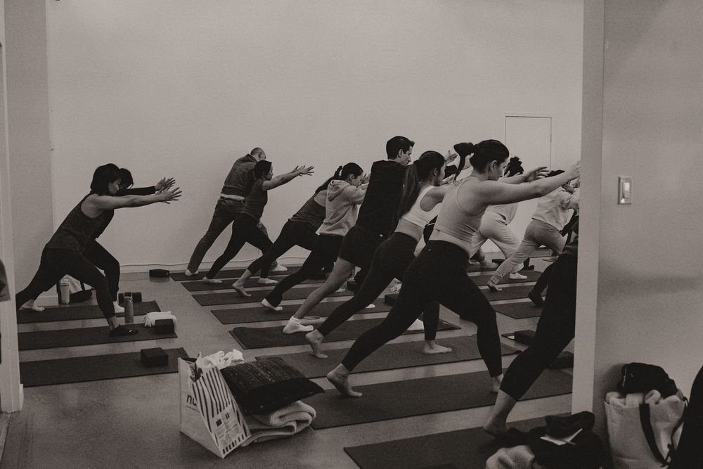 A black and white panorama shows people stretching and practicing yoga poses on mats in a fitness studio.