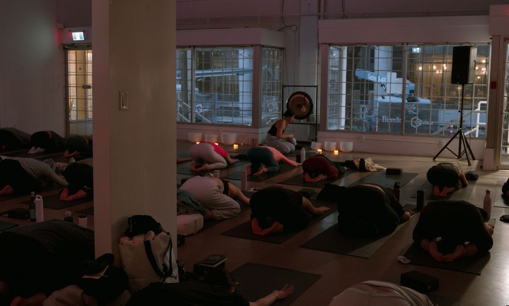 Group of people laying down in a dimly lit studio space during what appears to be a meditation or relaxation session.