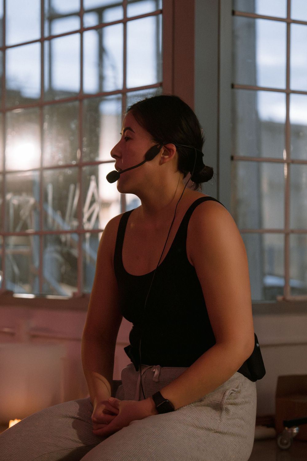 Instructor wearing headset microphone teaches class in sunlit studio setting with large windows.