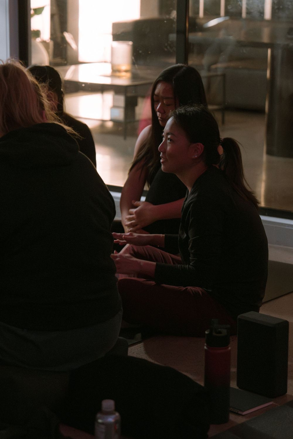 Students gathered in casual discussion in darkened studio space with sunlight streaming through windows.