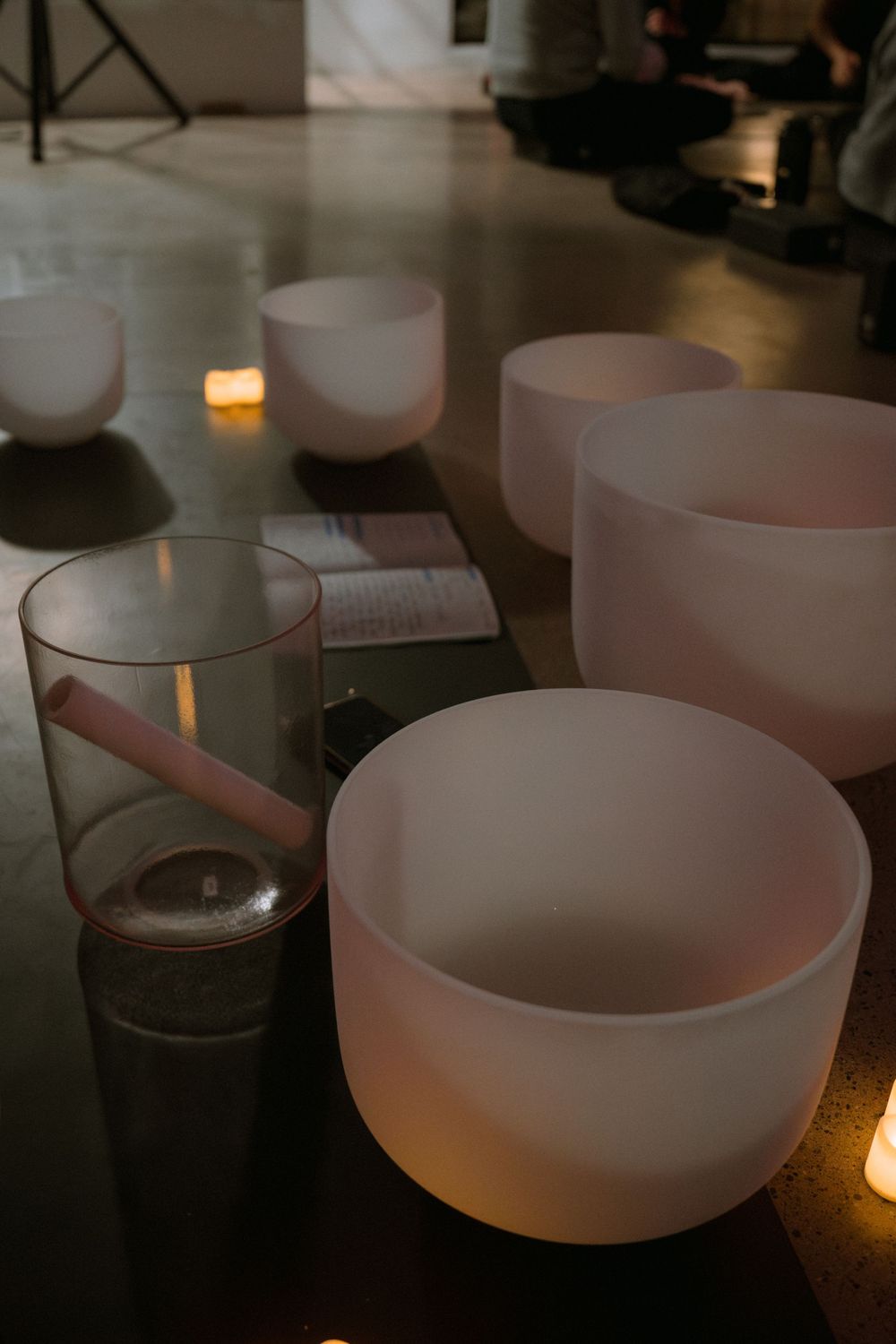 White crystal singing bowls glowing with warm candlelight in a dimly lit meditation space.