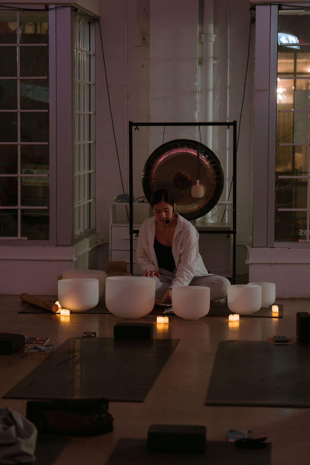 Peaceful meditation session setup with white singing bowls and candles arranged on floor in studio at dusk.