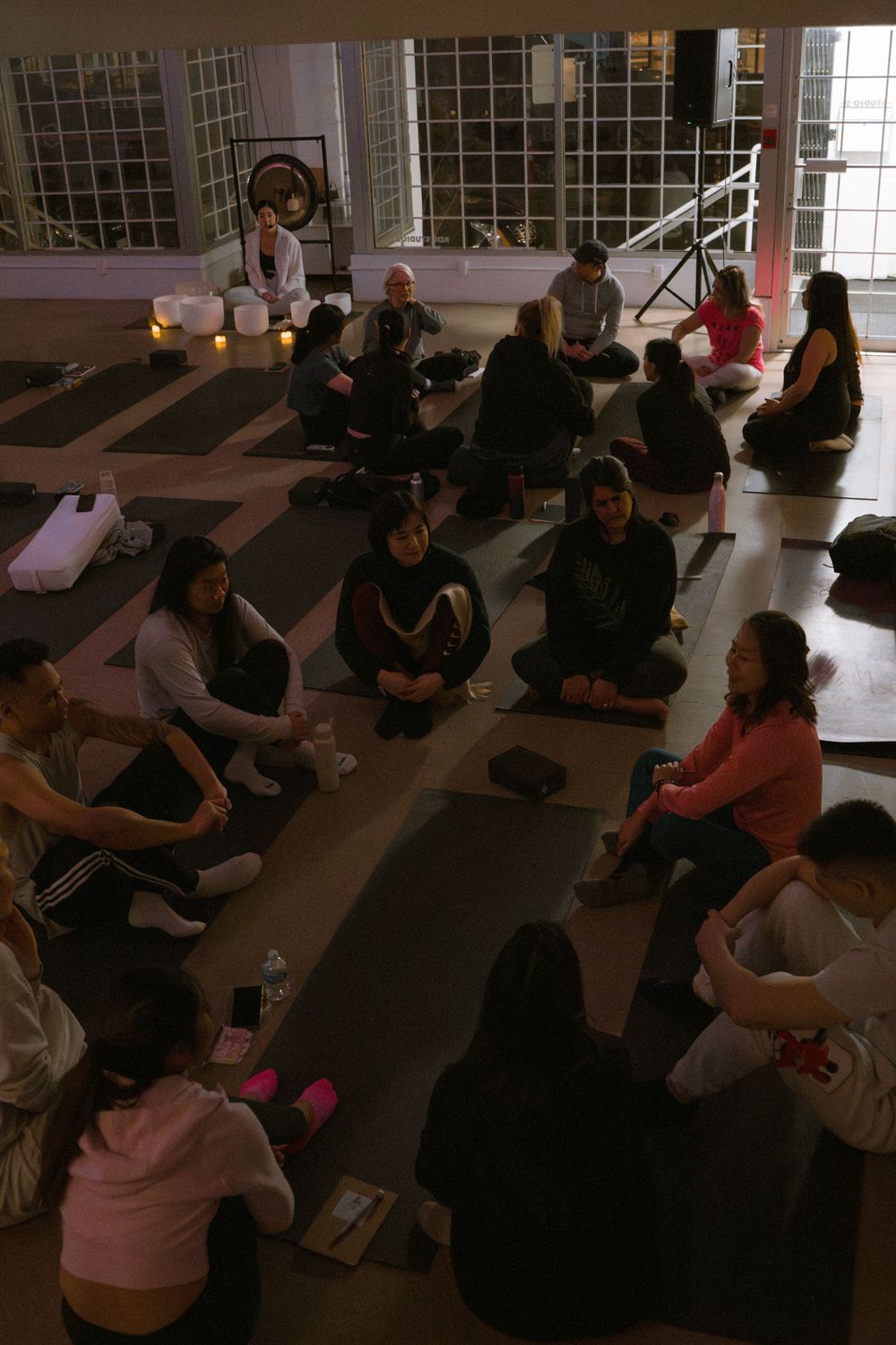 Group meditation session in a studio space with people sitting on yoga mats in dim lighting.