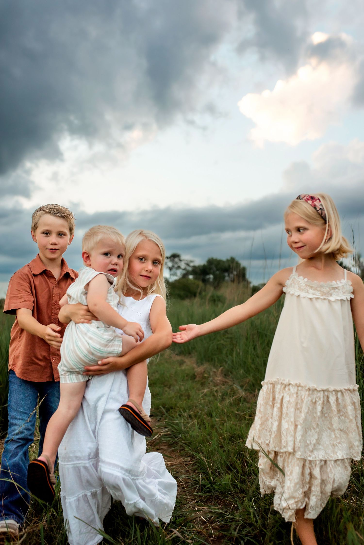 Children playing and laughing together in a field under dramatic stormy clouds at sunset.