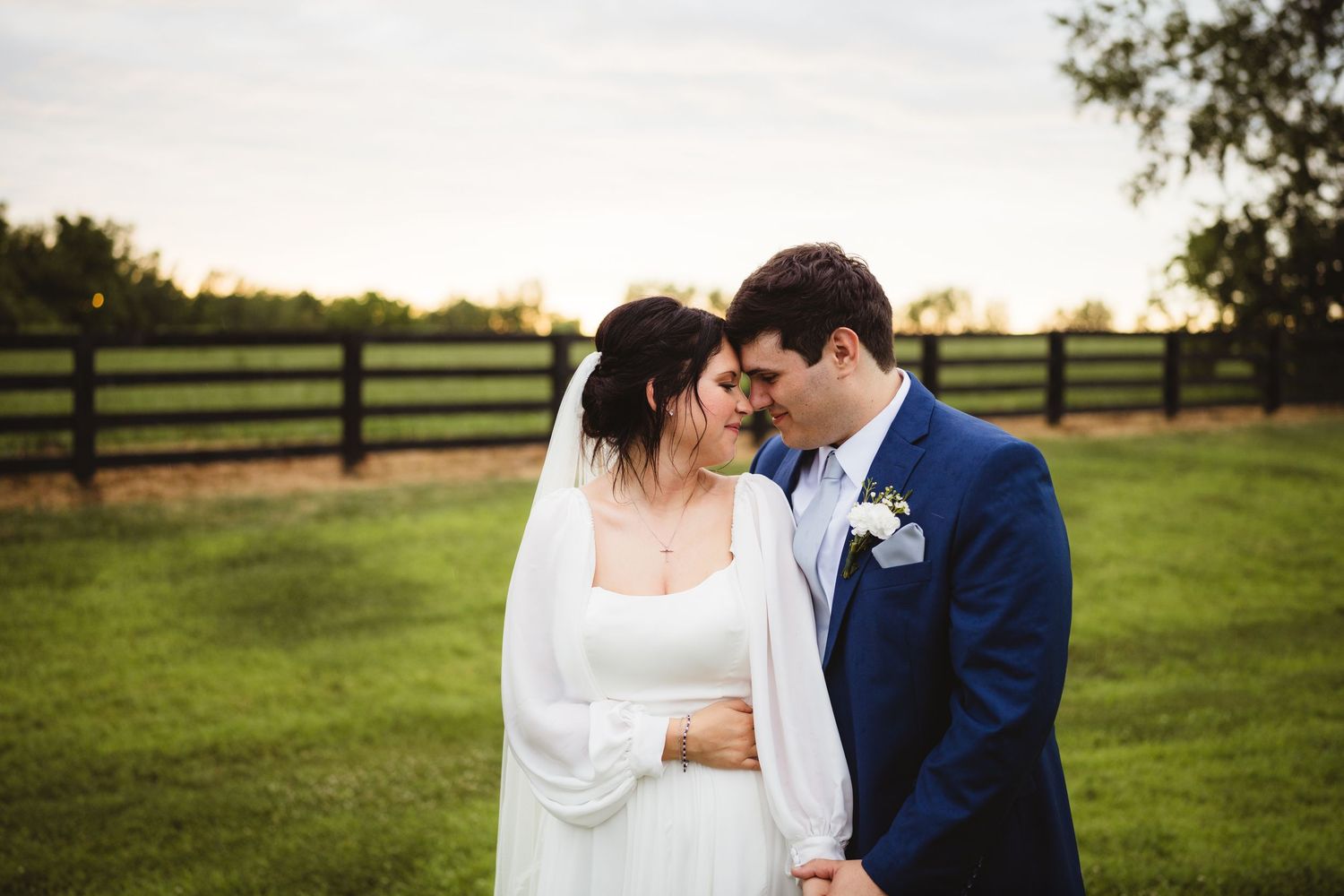 A bride and groom share intimate moments during an outdoor wedding photoshoot in a field at sunset.