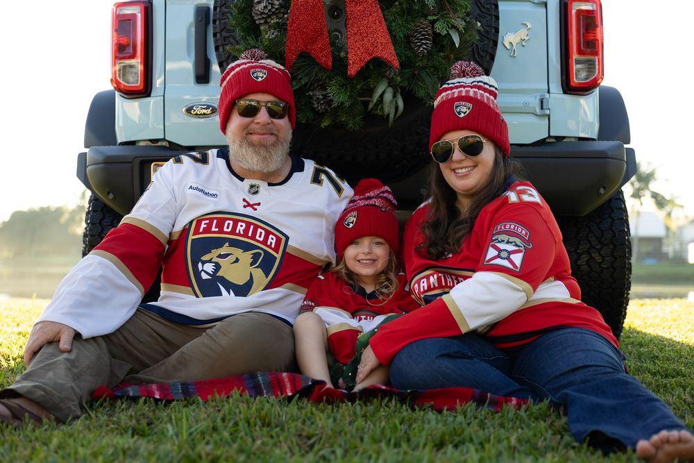 Group wearing red and white clothing posing by vehicle with holiday decorations.