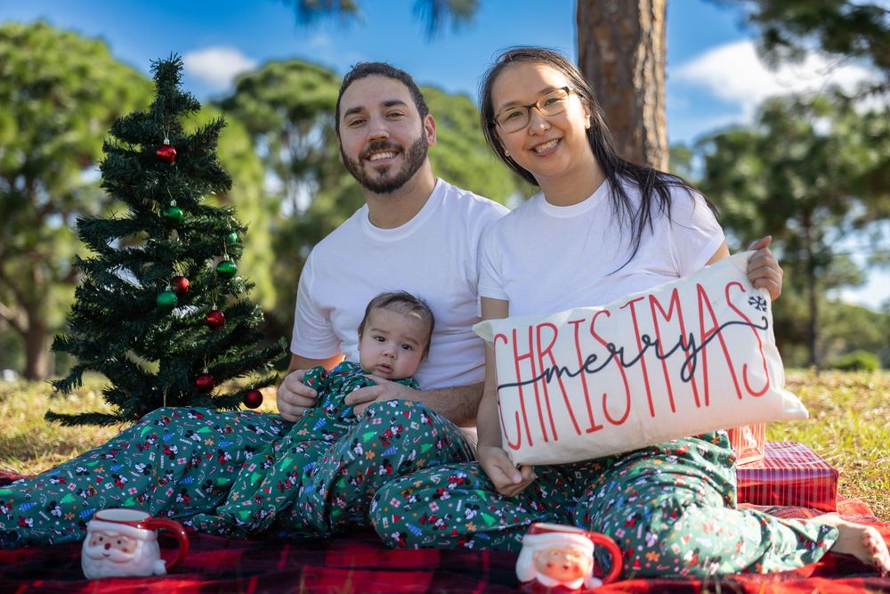 Family holiday photo session outdoors with Christmas tree and decorative signs.