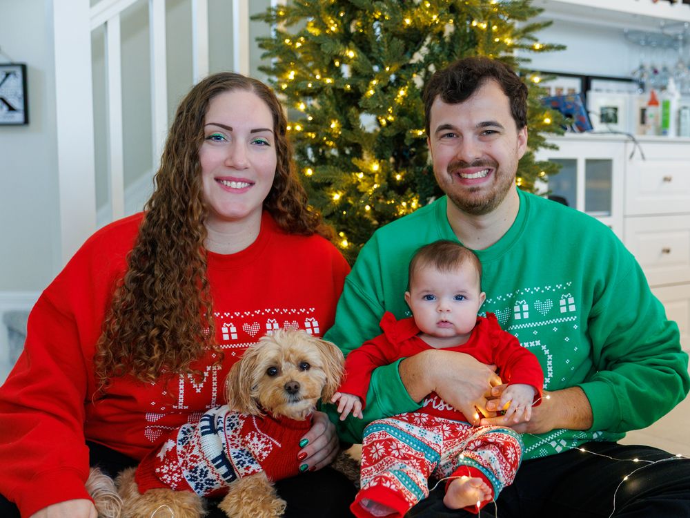 Family wearing matching Christmas sweaters poses together in front of decorated tree.